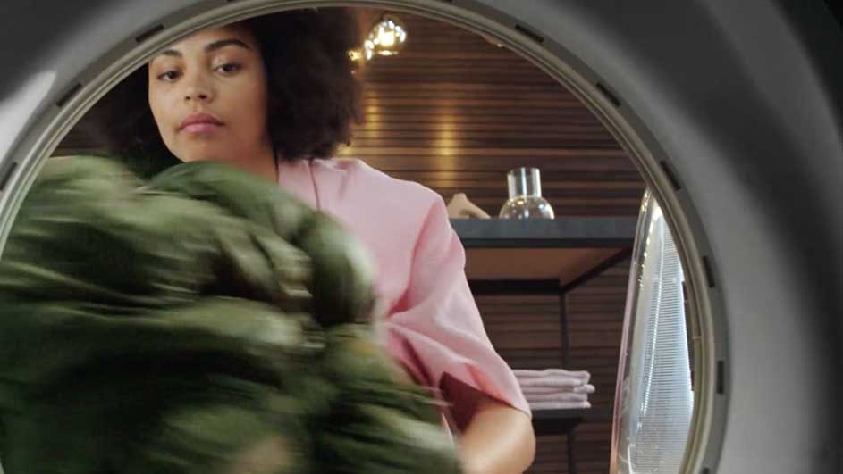 Vue d'un lave-linge, linge vert et étagère en arrière-plan.