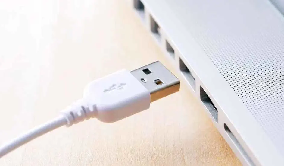 Een witte USB-A-connector wordt in een witte laptop gestoken op een houten ondergrond.