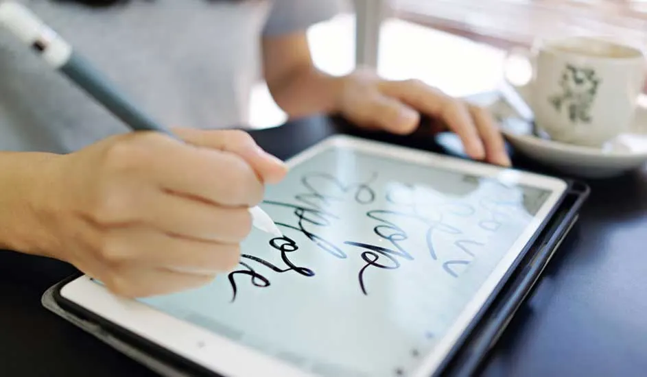 Hand schrijft op een tablet met een stylus. Kopje op een schotel staat op de achtergrond.