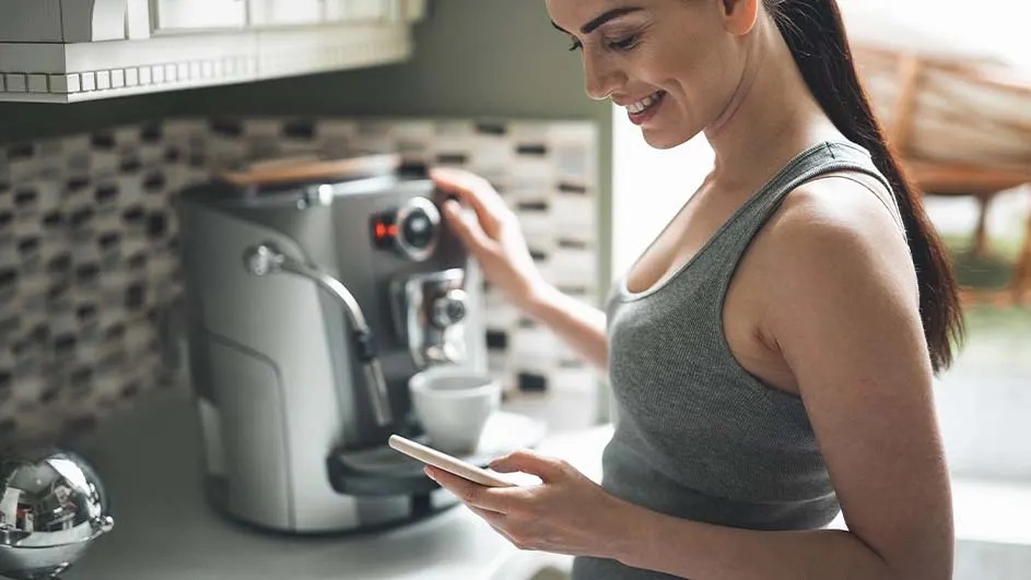 A white and black coffee machine with an open lid revealing coffee beans. The control panel has buttons for different drinks.