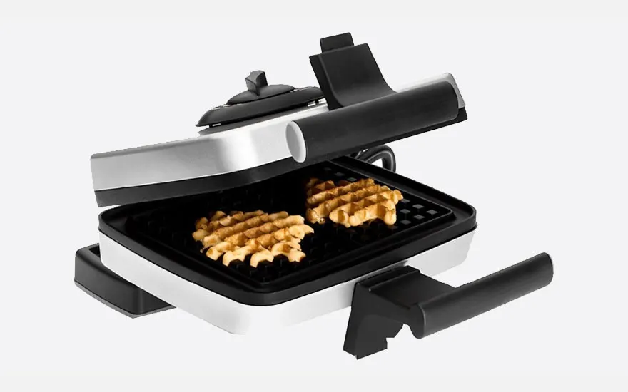 Een wafelijzer, open, met twee goudbruine wafels op een zwart rooster. Het apparaat is wit met zilveren details.