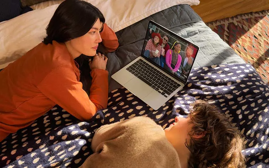 Une femme et un enfant sont allongés sur un lit sous une couverture douce et regardent ensemble une émission sur un ordinateur.