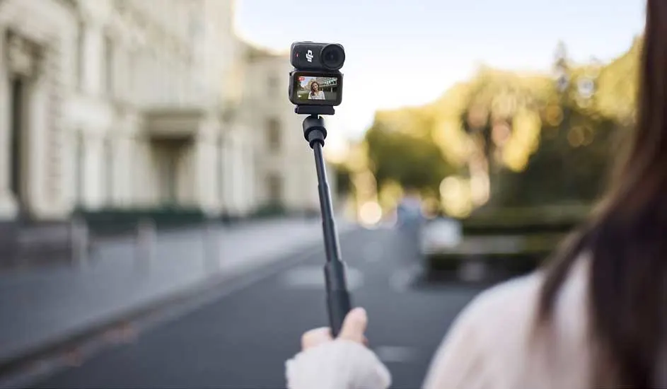 Une personne se filme dehors avec une caméra d’action DJI sur une perche, l’écran affiche le visage de l’utilisateur.