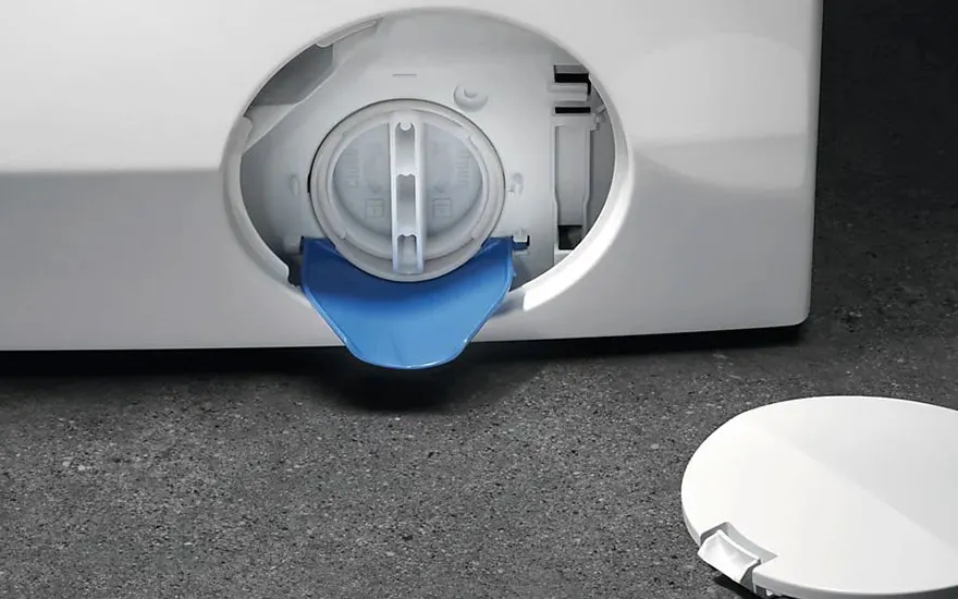 Wasmachine detail: witte machine met open filterklep en blauwe afvoertuit. Witte deksel ernaast op een grijze ondergrond.