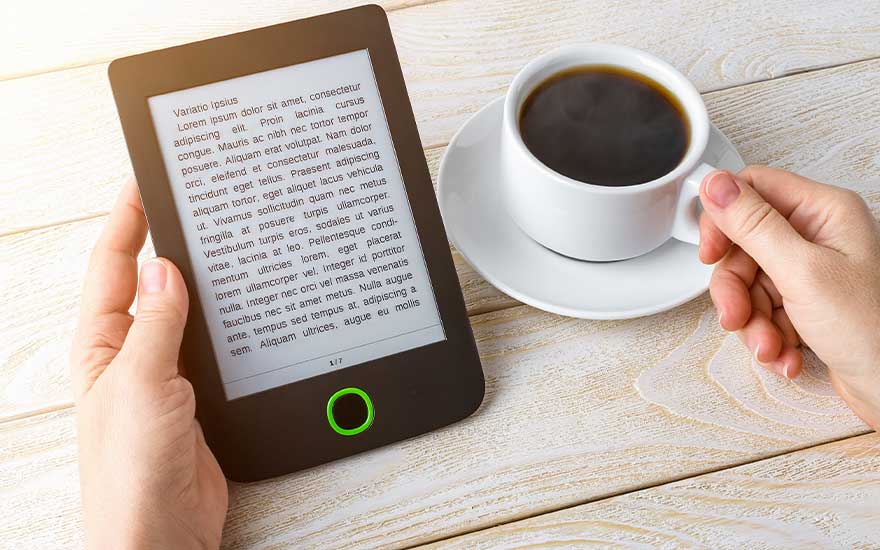 Een e-reader met tekst, een witte koffiekop met zwarte koffie op een schotel, en een houten tafel.