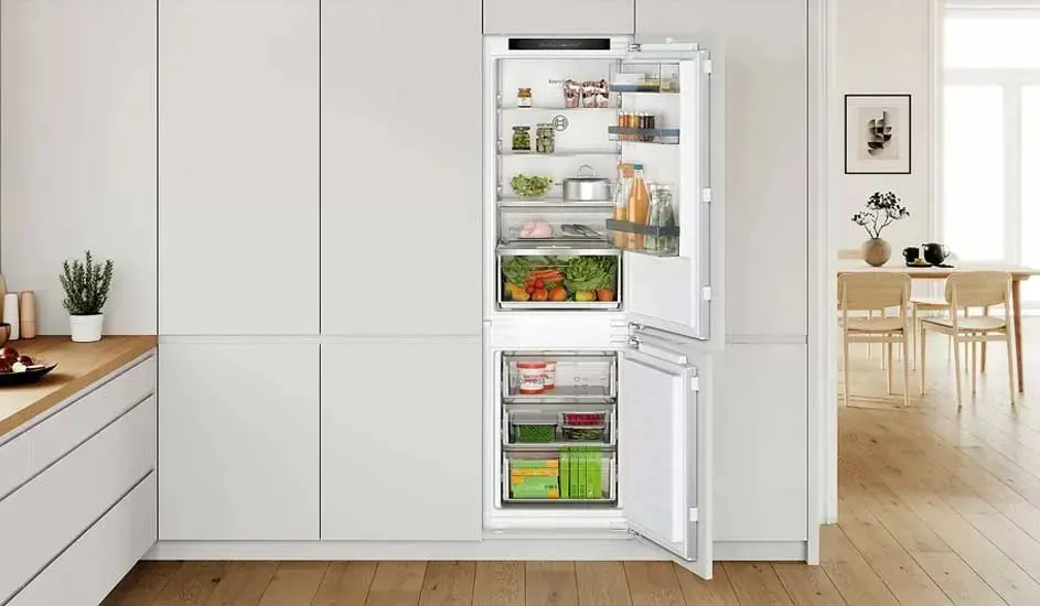 Un réfrigérateur blanc intégré est ouvert, révélant des étagères remplies de fruits, de légumes et de boissons.