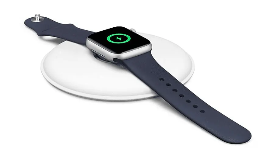 Een smartwatch met een blauw bandje ligt op een witte draadloze oplader. Het scherm toont een groen oplaadpictogram.