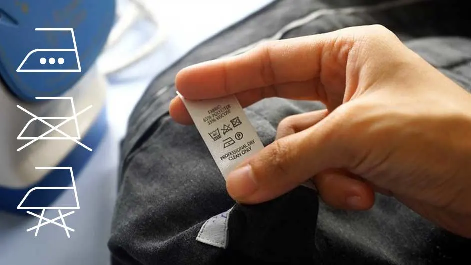 Hand houdt een waslabel vast aan een grijs kledingstuk. Strijkijzer-symbolen staan links.