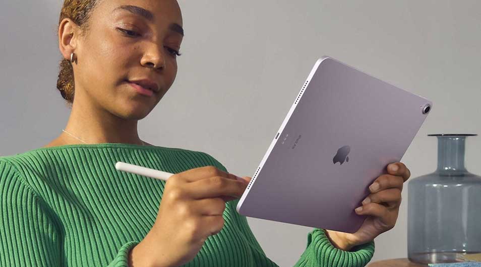 Une tablette violette est tenue avec un stylet blanc. Un vase en verre bleu est visible en arrière-plan, sur une table.