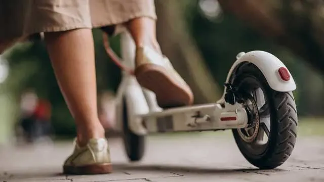 Een witte elektrische step staat op een tegelpad. Een voet staat op de step, de andere op de grond.