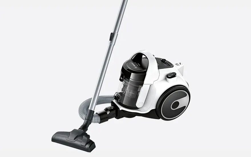 White cylinder vacuum cleaner with black transparent dust container, flexible hose and metal tube with wide floor nozzle on a neutral background.