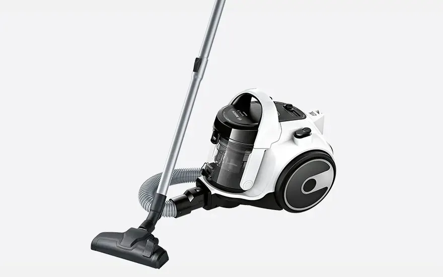 White cylinder vacuum cleaner with black transparent dust container, flexible hose and metal tube with wide floor nozzle on a neutral background.
