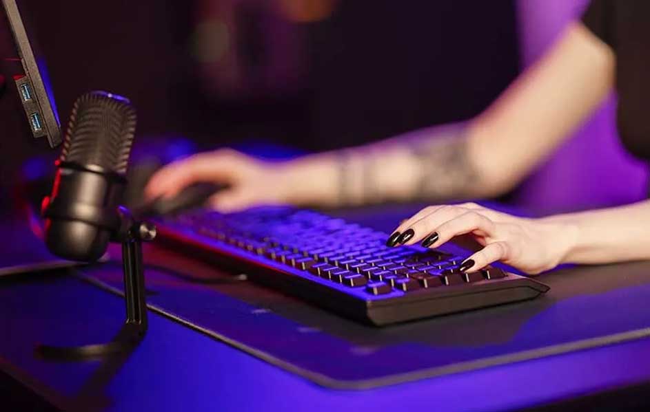 Un microphone noir sur un bureau bleu, avec un clavier noir et un écran d'ordinateur.