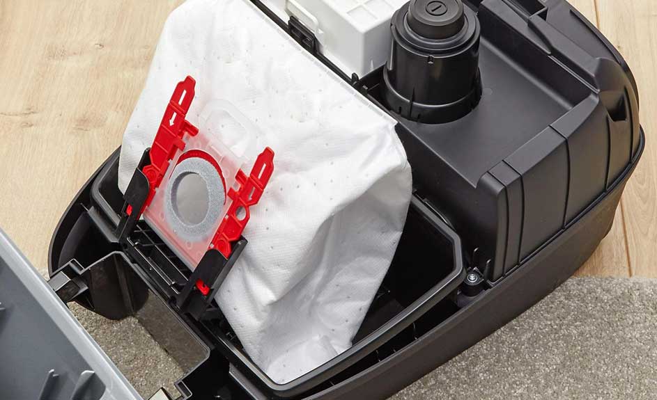 Vue rapprochée d'un aspirateur noir avec un sac blanc fixé par des supports rouges.