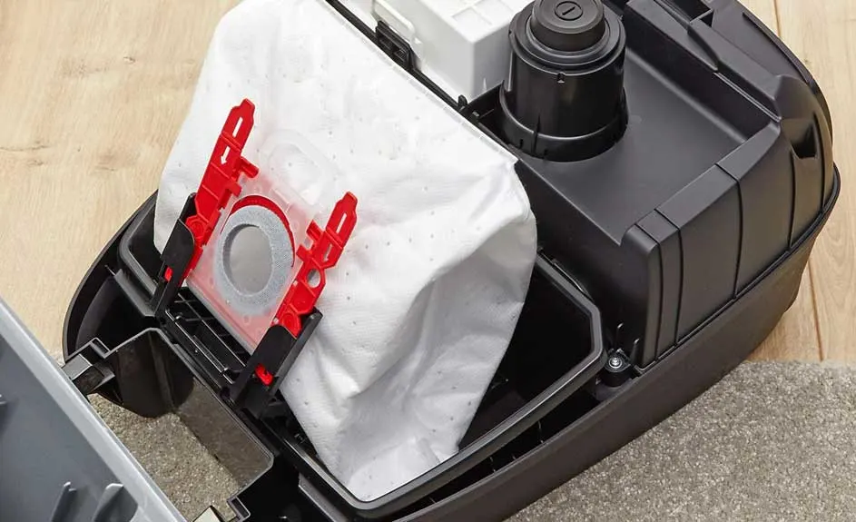Vue rapprochée d'un aspirateur noir avec un sac blanc fixé par des supports rouges.