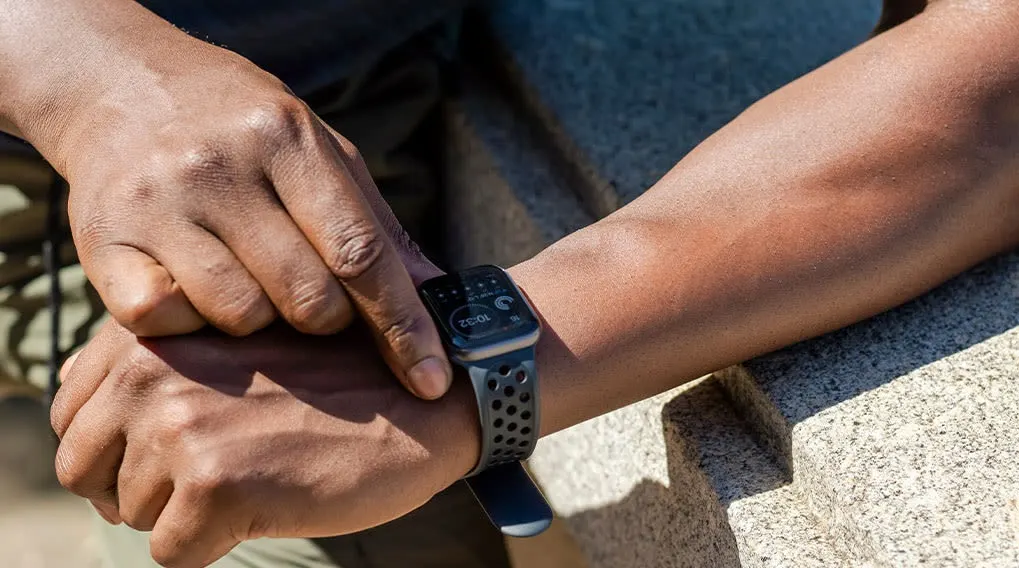 Een smartwatch met een zwarte band toont 10:32 op een pols naast een hand. De achtergrond is vaag.