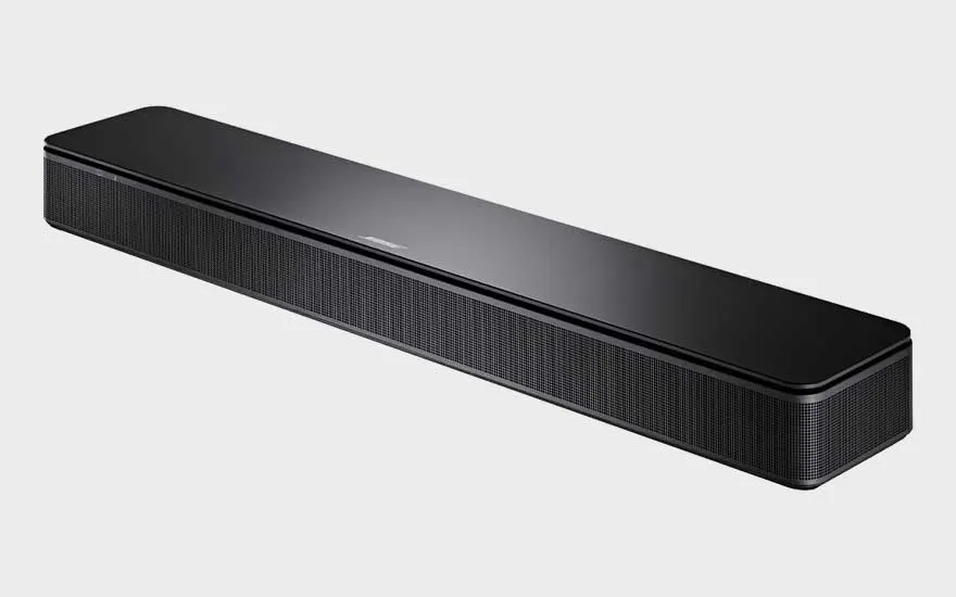 Une barre de son Bose noire brillante est photographiée en gros plan et en biais sur fond clair, avec une fine grille frontale.