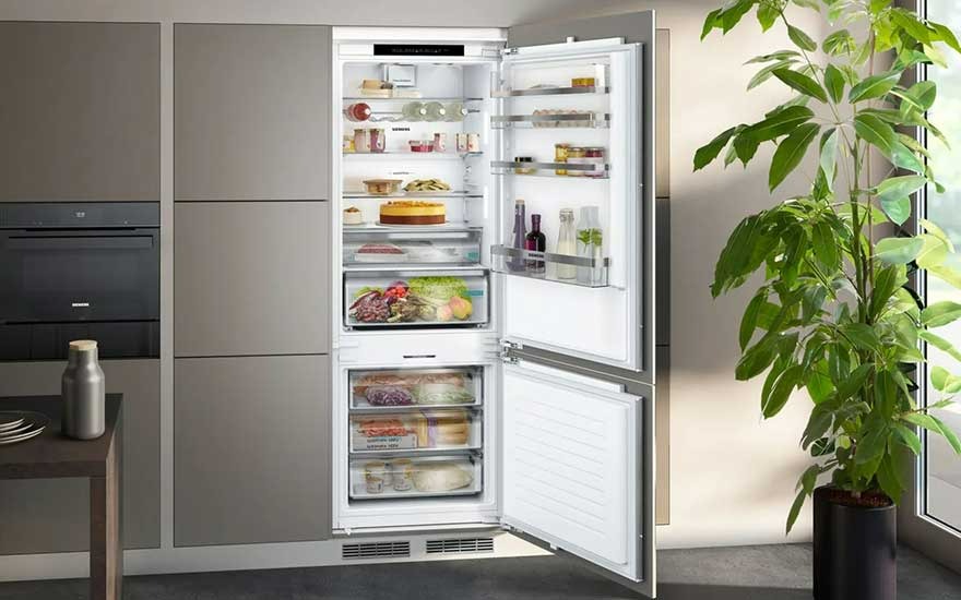 Un réfrigérateur blanc ouvert rempli de nourriture, à côté d'une plante verte en pot dans une cuisine moderne.