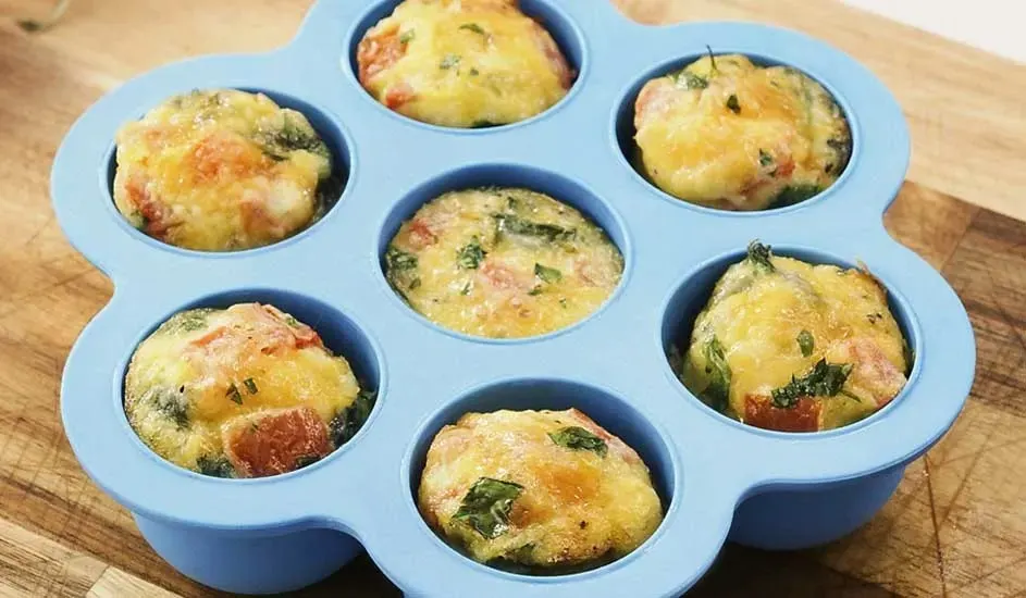 Zeven hartige muffins met groenten en kaas in een blauwe siliconen bakvorm, geen merk zichtbaar.