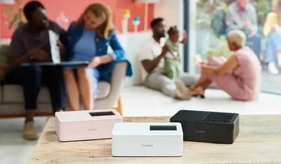 Drie Canon printers (roze, wit en zwart) op tafel. Achtergrond: mensen in een woonkamer.