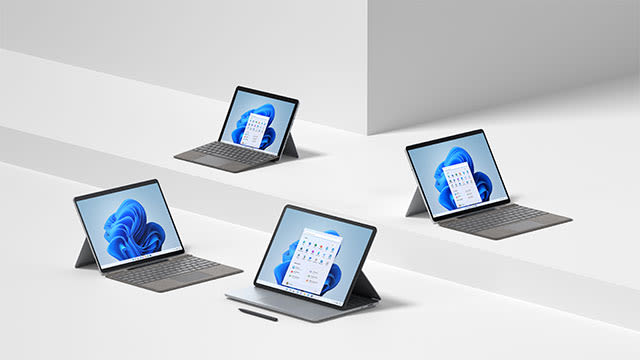 Quatre ordinateurs portables gris affichent Windows sur un fond blanc à plusieurs niveaux. Certains montrent un calendrier.