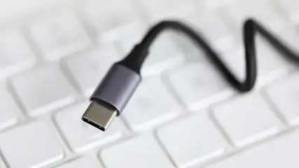 Een zwarte USB-C kabel ligt op een wit toetsenbord. De kabel heeft een grijze connector.
