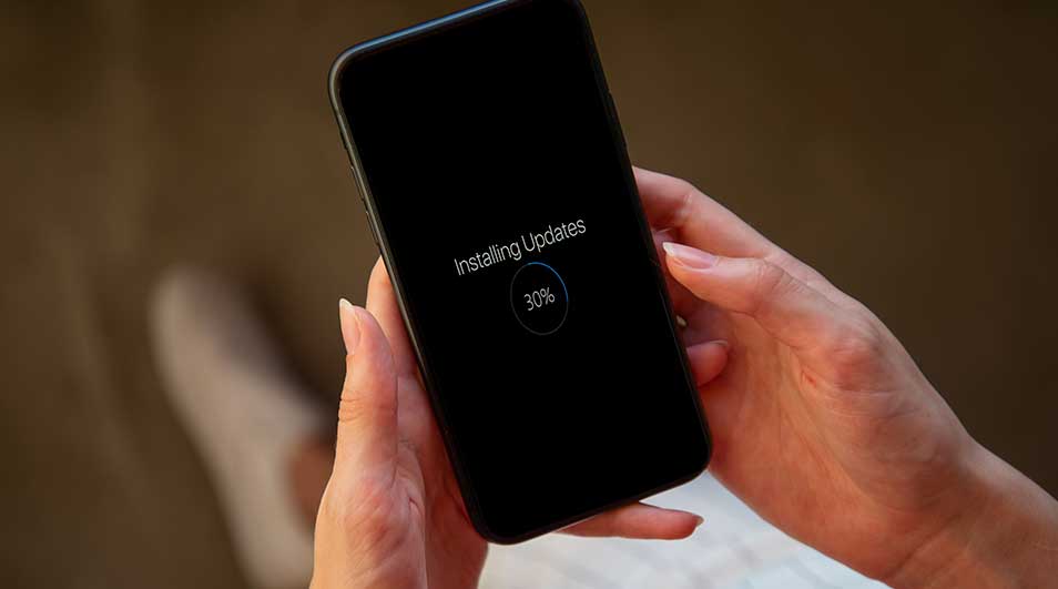 Un téléphone noir affiche "Installation des mises à jour" à 30 %, tenu par deux mains sur un fond flou.