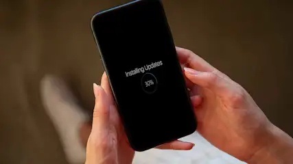 Zwarte smartphone in handen, updates installeren met 30% voltooid, tegen een bruine achtergrond.