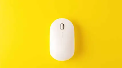 Une souris blanche d'ordinateur est posée sur un fond jaune uni. La souris est centrée et orientée verticalement.