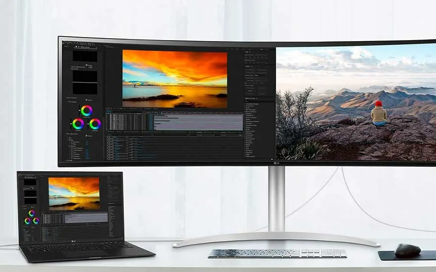 Een bureau toont een laptop en een ultrabrede monitor met bewerkingssoftware. Het scherm toont landschappen en kleurtools.