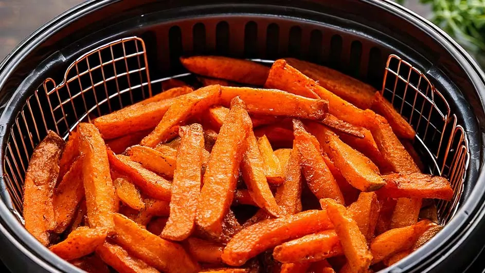 Un panier métallique rempli de frites de patates douces orange. Le panier est dans une friteuse à air noire.