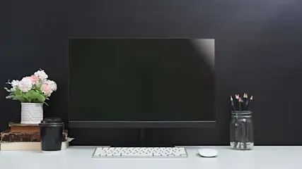 Bureau blanc avec écran, clavier, souris, fleurs, livres, café et crayons sur fond noir.