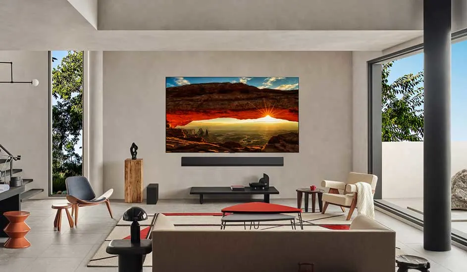 Een woonkamer met een tv waarop een rotsformatie te zien is bij zonsopgang. Er is veel natuurlijk licht.