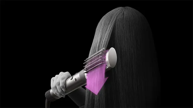 Une main tient une brosse à cheveux stylisante sur des cheveux longs. Une flèche violette indique le mouvement de la brosse. Fond noir.