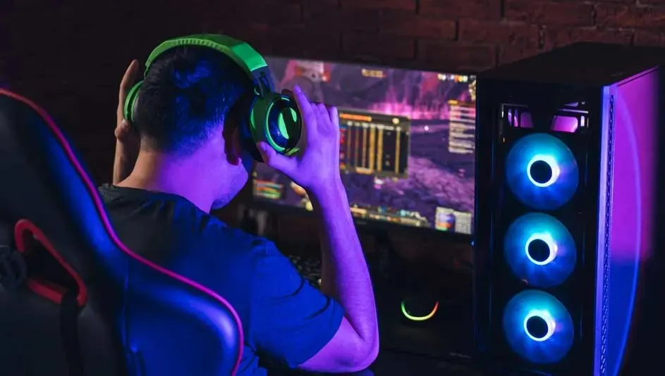 Een desktopcomputer met RGB-ventilatoren staat naast een scherm met gamebeelden, en een hoofdtelefoon.