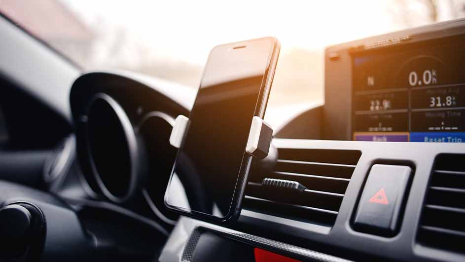 Un smartphone noir dans un support blanc sur le tableau de bord d'une voiture, près d'un écran et d'une grille d'aération.
