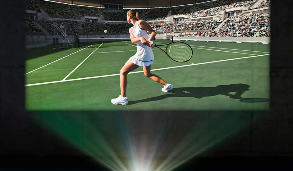 A tennis match is projected on a wall, showing a player in action on the court. A projector beams light to the screen. No brand is visible.