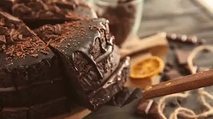 Des brownies au chocolat avec glaçage, des copeaux, une tranche d'orange et un couteau en bois sur une planche à découper.