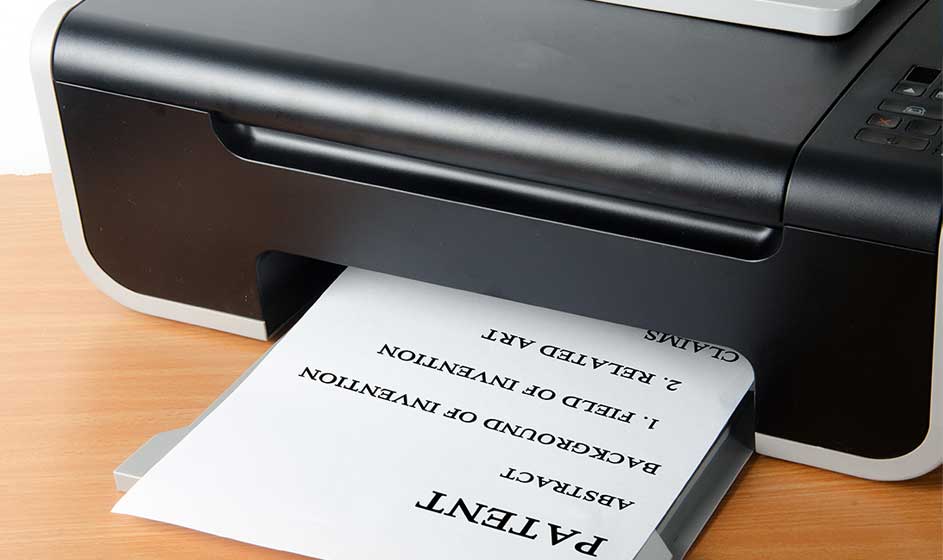 Une imprimante noire compacte fait sortir une feuille de papier. Le document présente des mots inversés et des lignes, posé sur un bureau en bois.