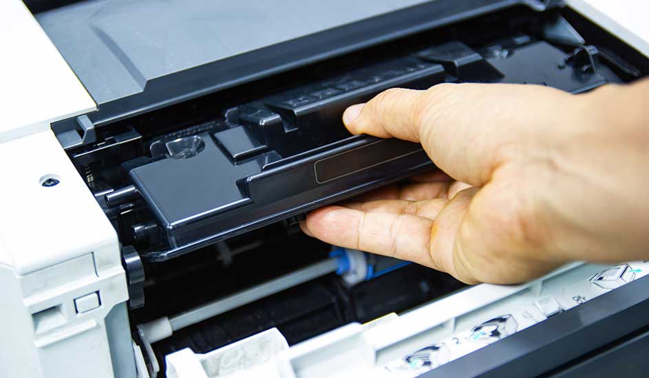 Een hand verwijdert een zwarte tonercartridge uit een witte en zwarte printer. Binnenkant zichtbaar.