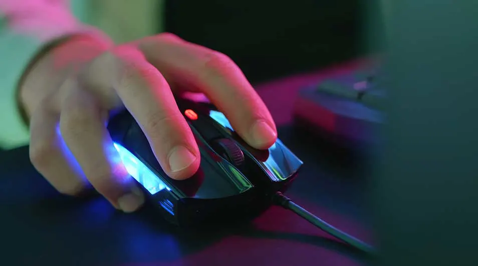 Een hand op een zwarte, verlichte computermuis met een scrollwiel op een donkere ondergrond.