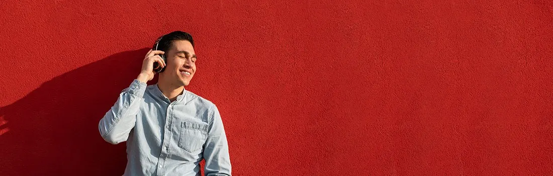 A person in a blue shirt wears headphones against a solid red textured wall.
