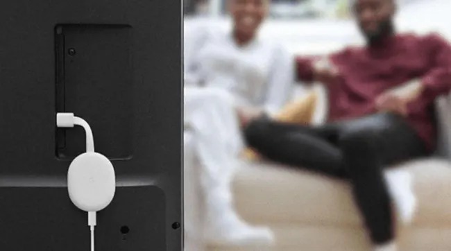 Téléviseur noir avec appareil blanc connecté. Un couple est assis sur un canapé en arrière-plan.