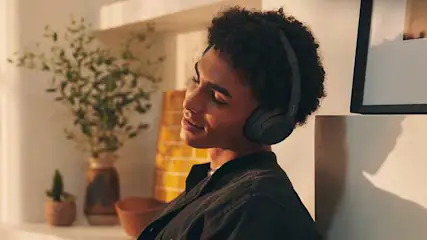 Une pièce éclairée avec des plantes, un vase et une photo encadrée. Un casque audio noir est visible au premier plan.