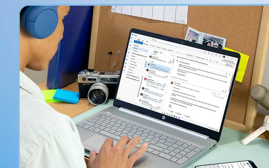 Une personne assise à un bureau, portant des écouteurs bleus, utilise un ordinateur portable HP avec une application de messagerie ouverte, entourée d'accessoires de bureau classiques.