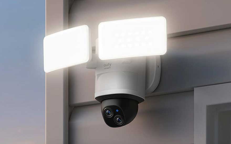 Witte beveiligingscamera met twee heldere lampen gemonteerd op een grijze muur. De camera heeft een zwarte lens.