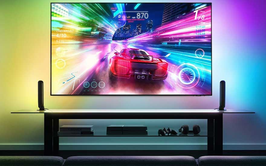 Téléviseur affichant une course automobile sur une console multimédia noire avec des haut-parleurs et des lumières d'ambiance colorées.