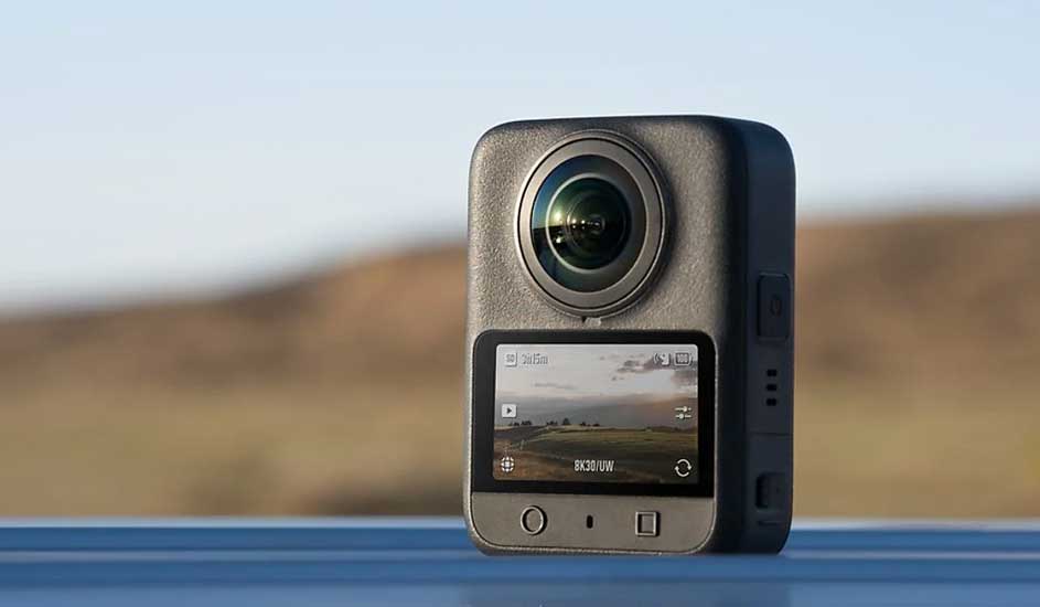 Een zwarte GoPro MAX 360 actiecamera met een groot rond objectief boven een kleurenscherm waarop een landschap wordt weergegeven.