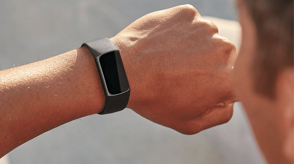 Poignet avec bracelet de suivi d'activité gris et écran noir, sur fond flou.