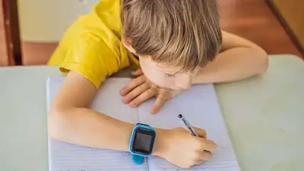 Een schrijver met een blauw horloge schrijft op papier op een witte tafel met een pen.